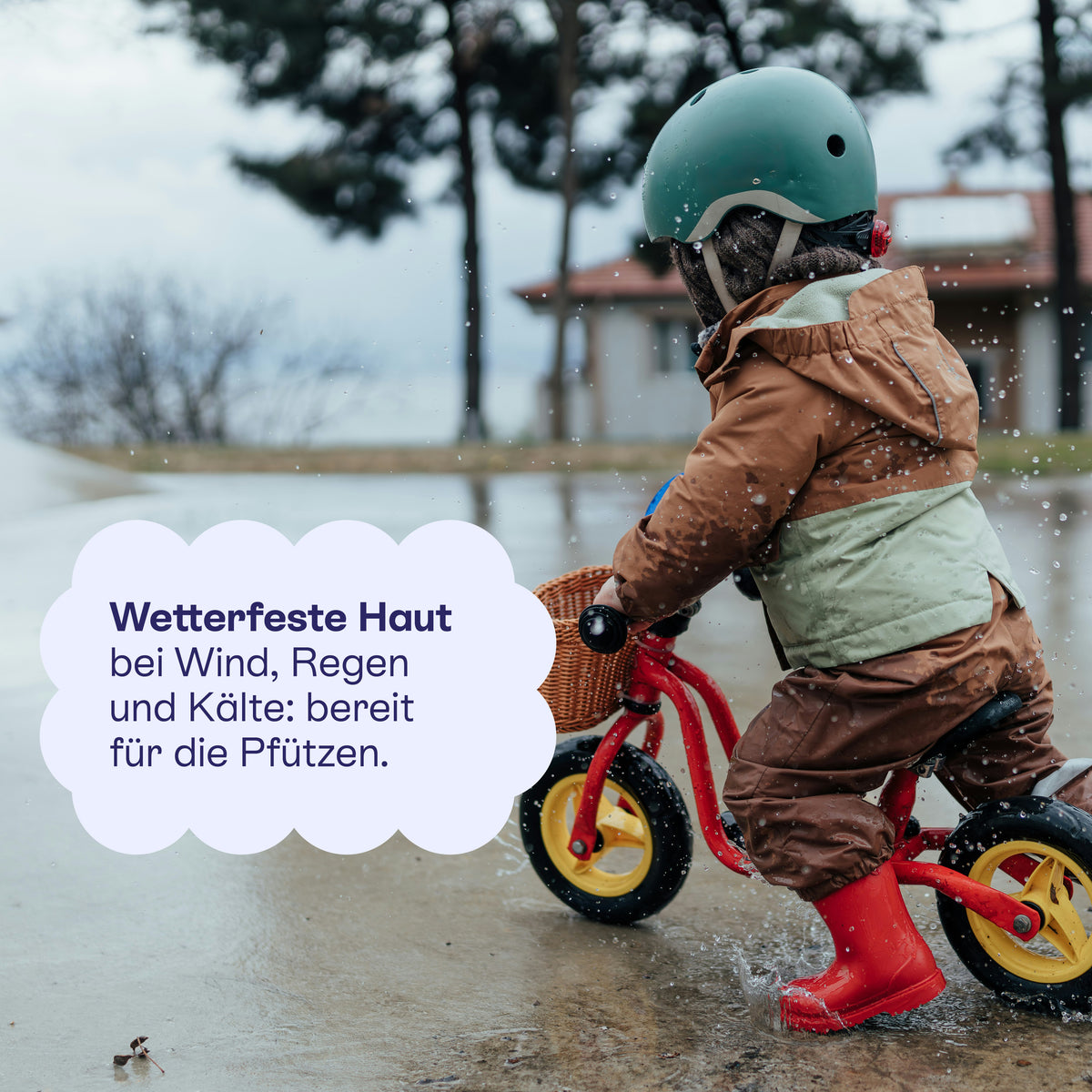 Kind mit Helm auf dem Laufrad im Regen: wetterfeste Haut für die Pfützen.