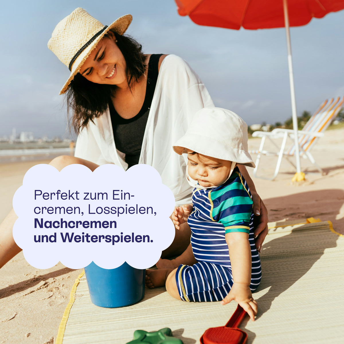 Mutter und Kind mit Sonnenhut am Strand, bereit zum Eincremen, Planschen und Spielen.
