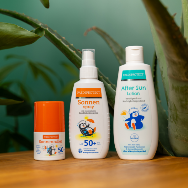 Der PAEDIPROTECT Sonnenroller, Sonnenspray und After SUn Lotion auf einem Tisch mit Aloe Vera im Hintergrund