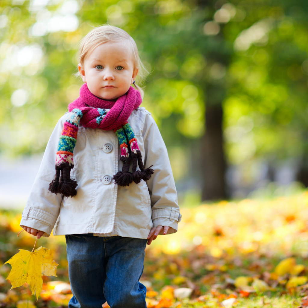 kleines Mädchen, das mit Jacke und Schal durch das Herbstlaub läuft